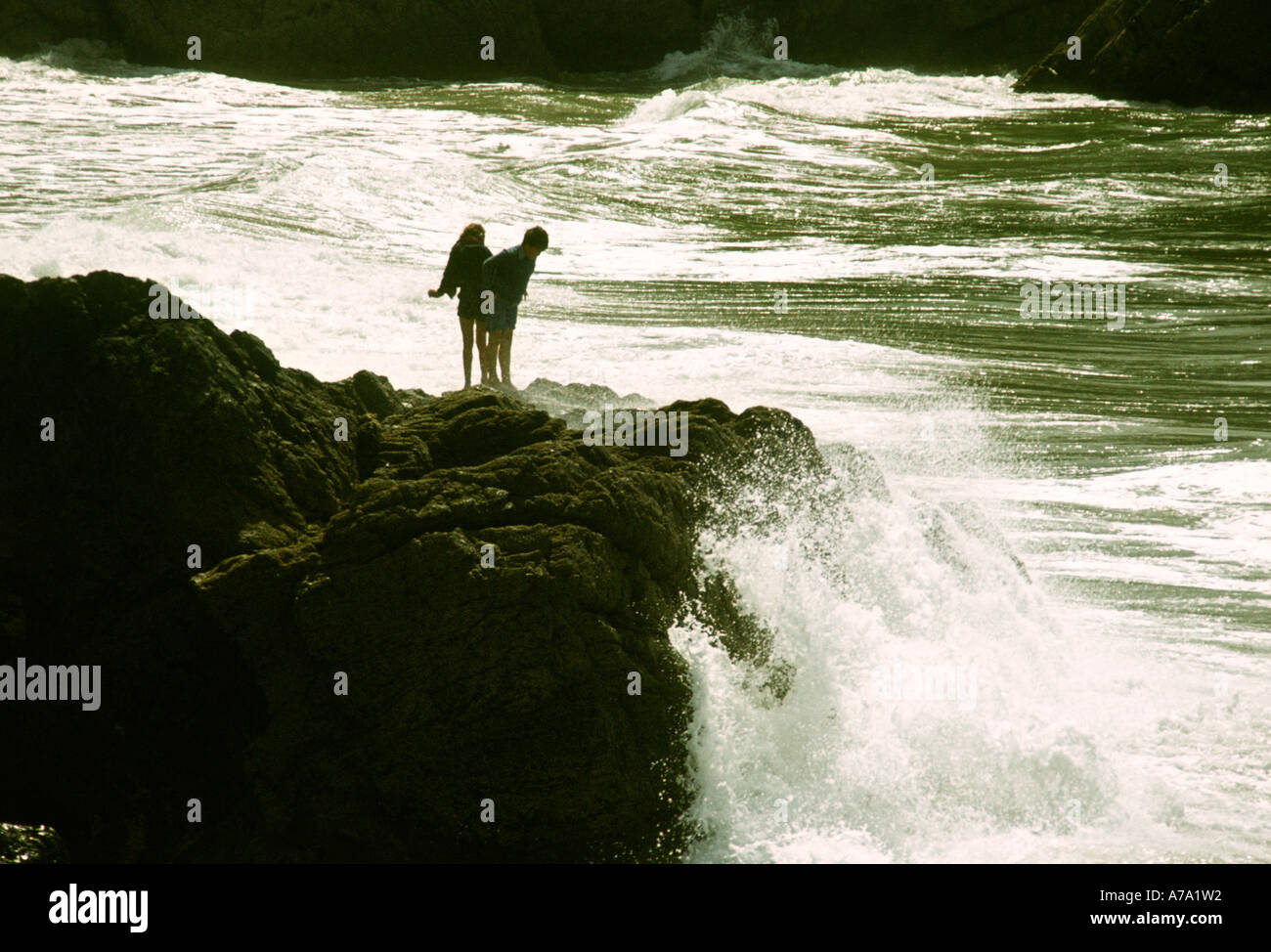 Cornwall Meneau enfants debout sur rock comme la mer s'écrase dans Banque D'Images
