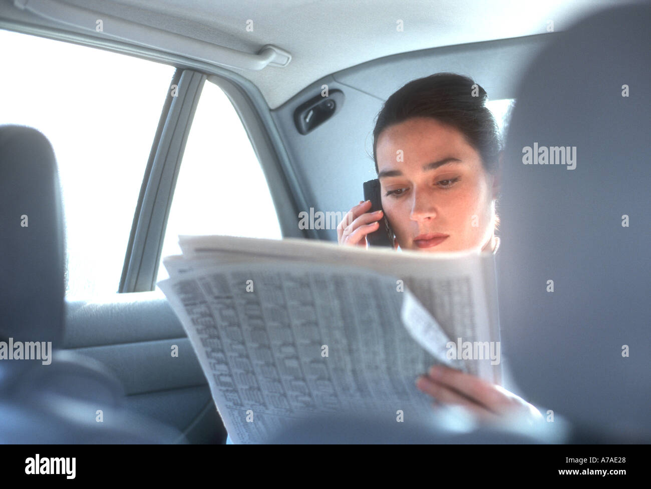 Woman on cell phone exécutif journal de lecture alors qu'en limousine Banque D'Images