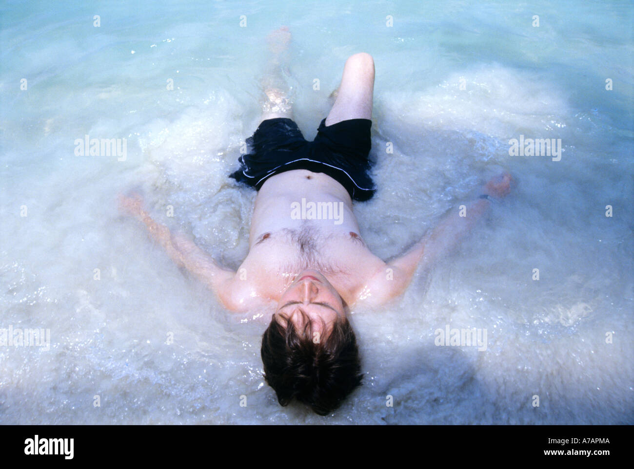 Jeune homme étendu dans l'eau peu profonde Banque D'Images