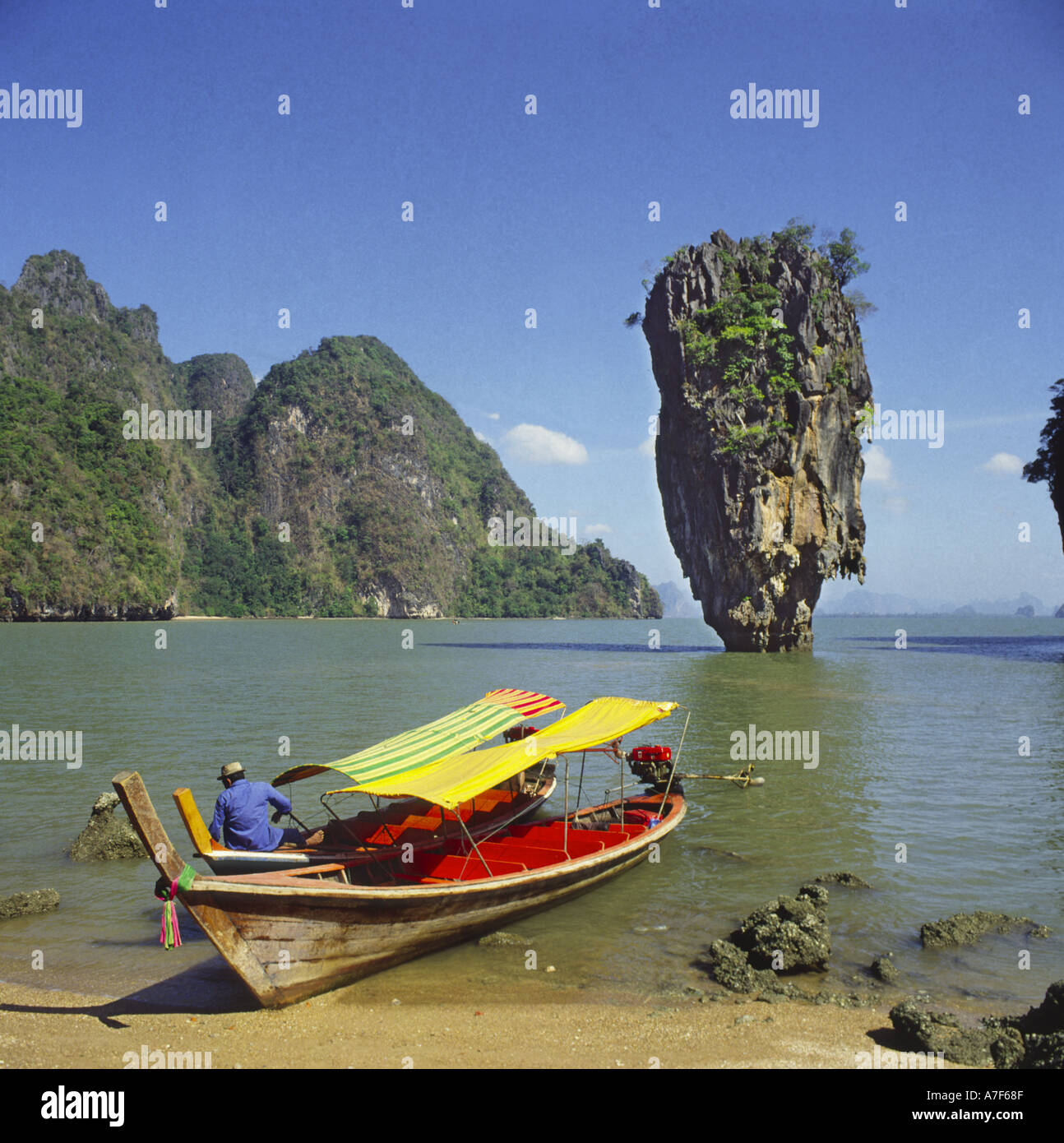 Deux bateaux thaïlandais et un marin à la plage avec pile de roche calcaire Ko Tapu Mont juste au large dans la baie de Phang Nga Bay Thaïlande Banque D'Images