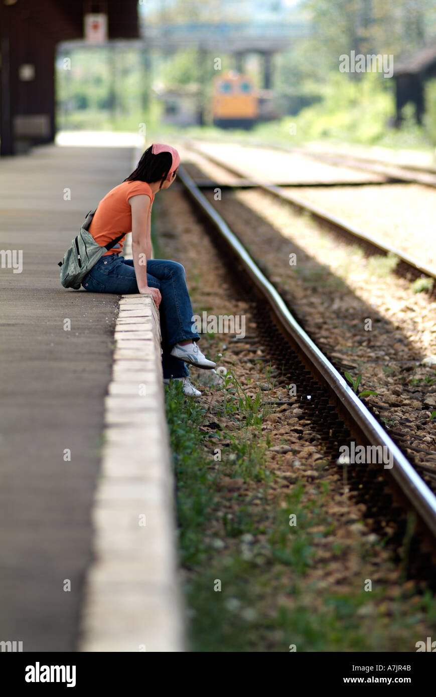 Femme assise sur une plate-forme du train à la recherche dans l'axe de la voie ferrée en prévision Banque D'Images
