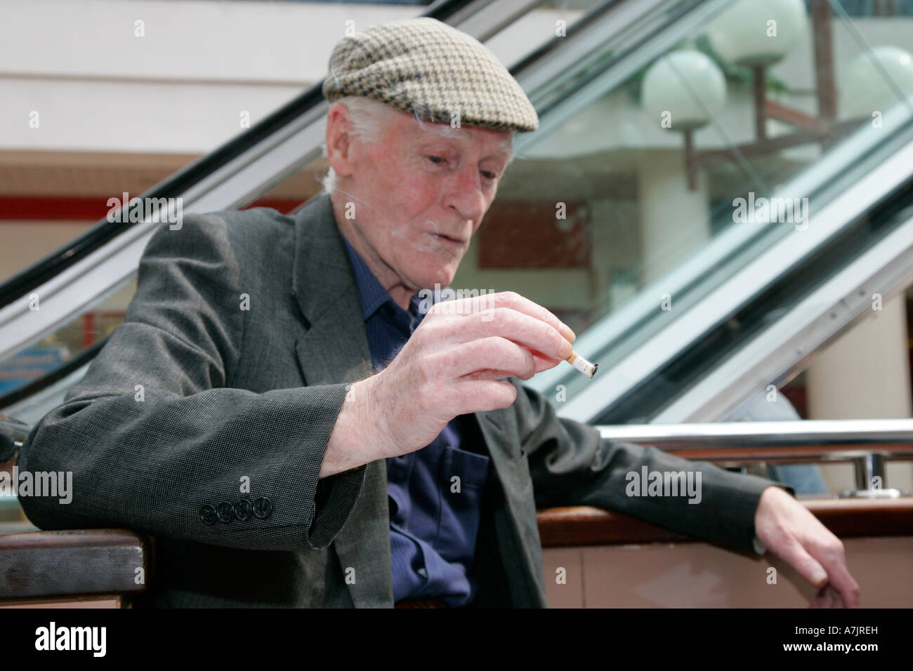 Un homme âgé avec casquette fumeurs holding out les restes d'une cigarette dans un centre commercial avant l'interdiction de fumer Banque D'Images