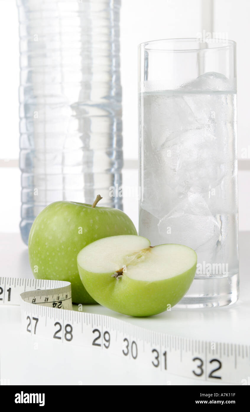 PORTRAIT D'UNE BOUTEILLE D'EAU AVEC UN VERRE D'EAU ET DEUX POMMES UN ENSEMBLE ET UNE COUPE DANS LA MOITIÉ avec un ruban à mesurer Banque D'Images