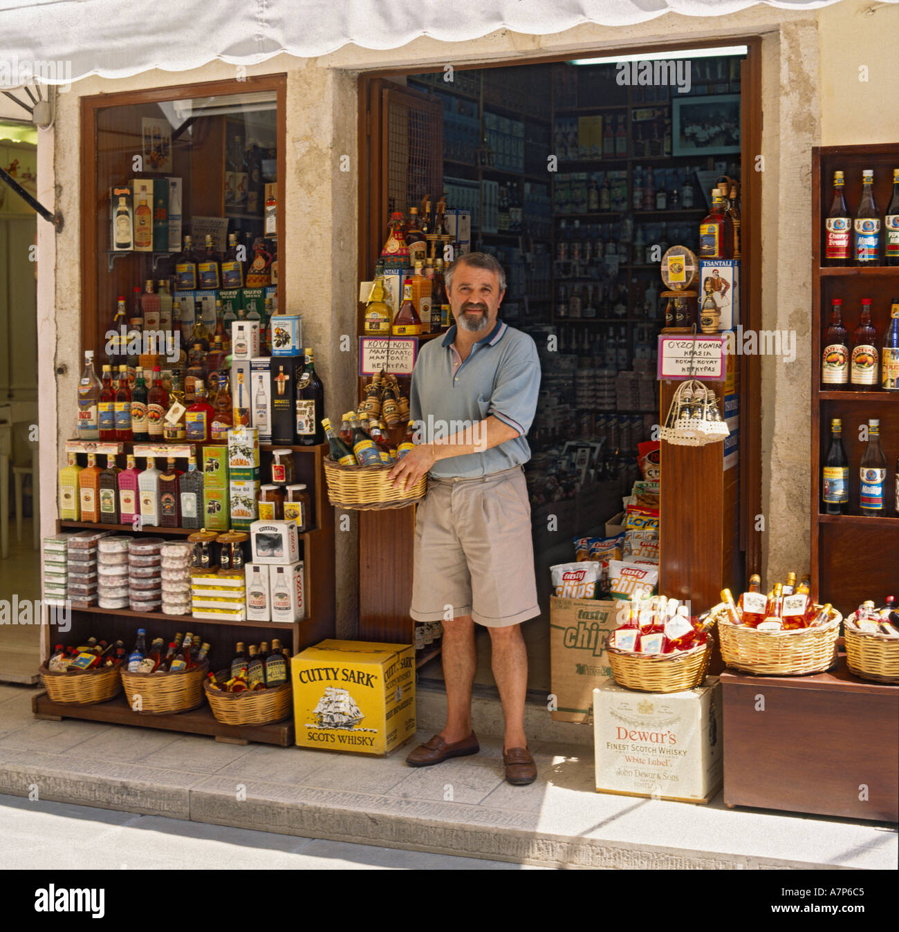 Propriétaire d'un magasin local regardant la caméra en plein soleil tôt le matin dans la rue étroite ville de Corfou îles Grecques Banque D'Images