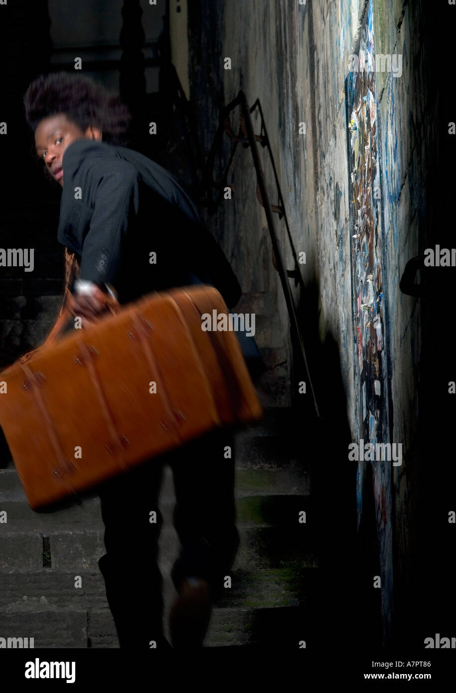 20 s de l'homme Afro Antillais courir vers le haut d'un escalier tenant une valise en cuir marron Banque D'Images