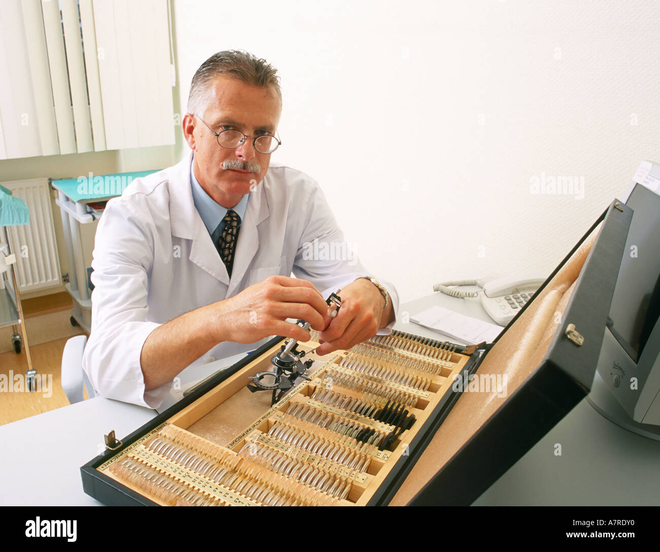 À l'intérieur du cabinet ambulatoire mature homme aux cheveux gris 4550 lunettes moustache médecin ophtalmologiste sit optomerist tiroir robe gl Banque D'Images