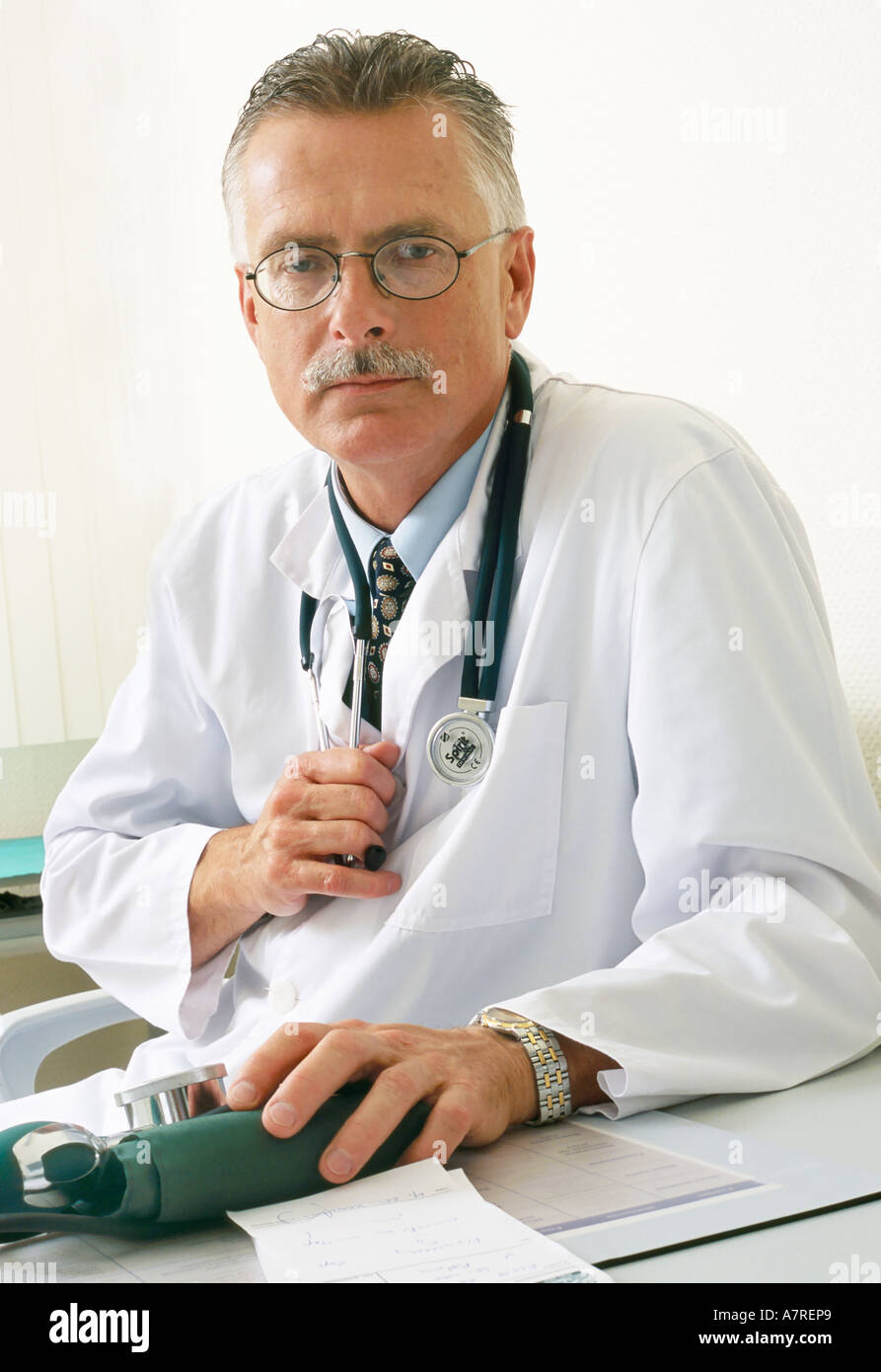 À l'intérieur du cabinet ambulatoire mature homme aux cheveux gris 4550 lunettes moustache assis médecin stéthoscope blouse hypertension pression Banque D'Images