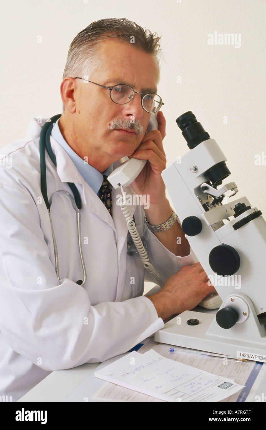 À l'intérieur du cabinet ambulatoire mature homme aux cheveux gris 4550 robe lunettes moustache stéthoscope médecin parler microscope Telephone Co. Banque D'Images
