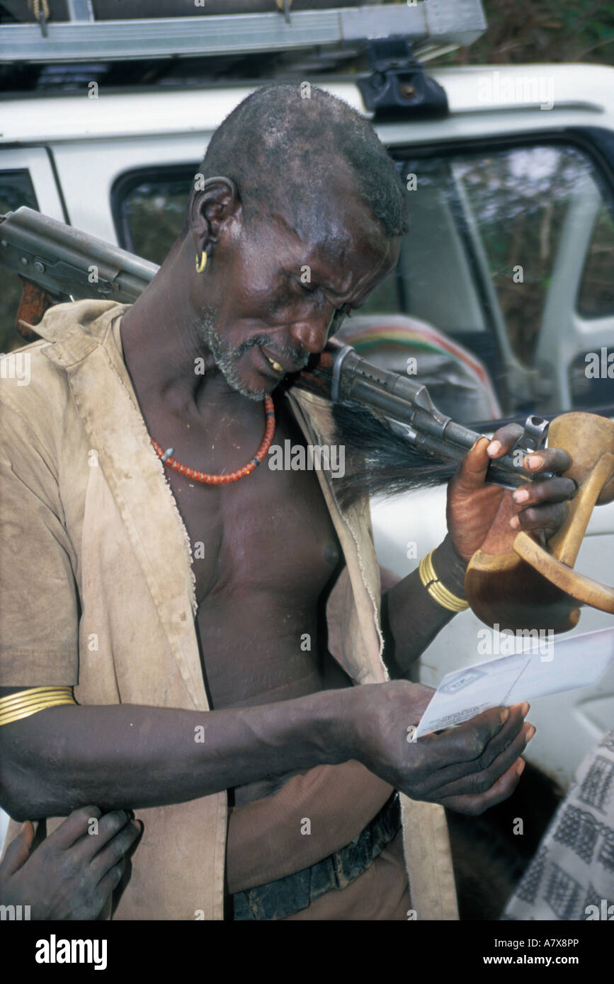 Rifle sur l'épaule, un homme Karo curieusement inspecte une carte postale américaine, près d'une voiture, dans la région de la rivière de l'Omo en Éthiopie Banque D'Images