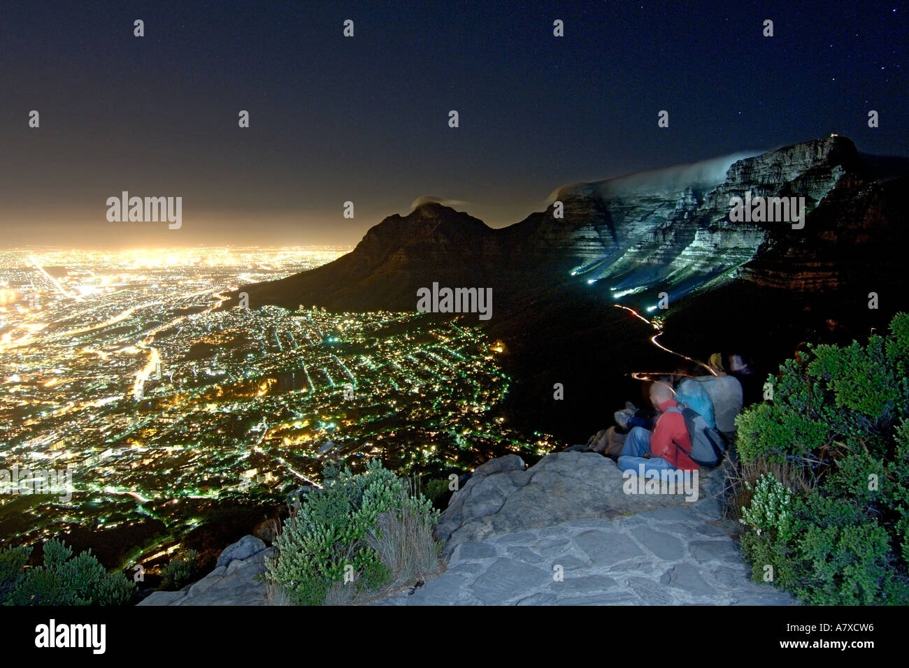 Un groupe de randonneurs s'asseoir sur le sommet de la tête de lion à admirer la montagne de la table et la ville du Cap sur une nuit de pleine lune. Banque D'Images