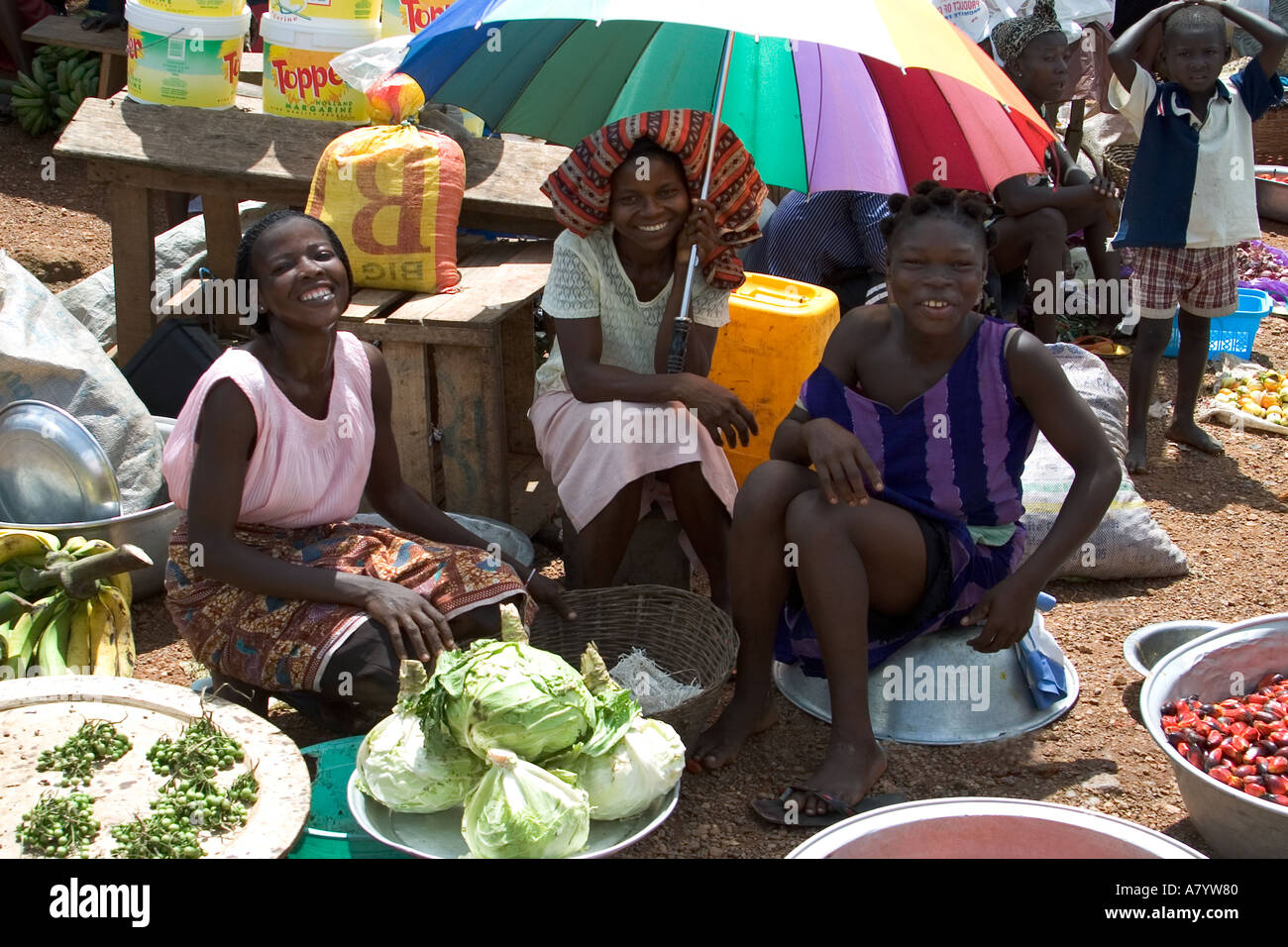 Marché alimentaire traditionnel en plein air en Afrique de l'Ouest avec des commerçants, avec 3 filles souriantes vendant des fruits et légumes dans la région occidentale du Ghana Banque D'Images