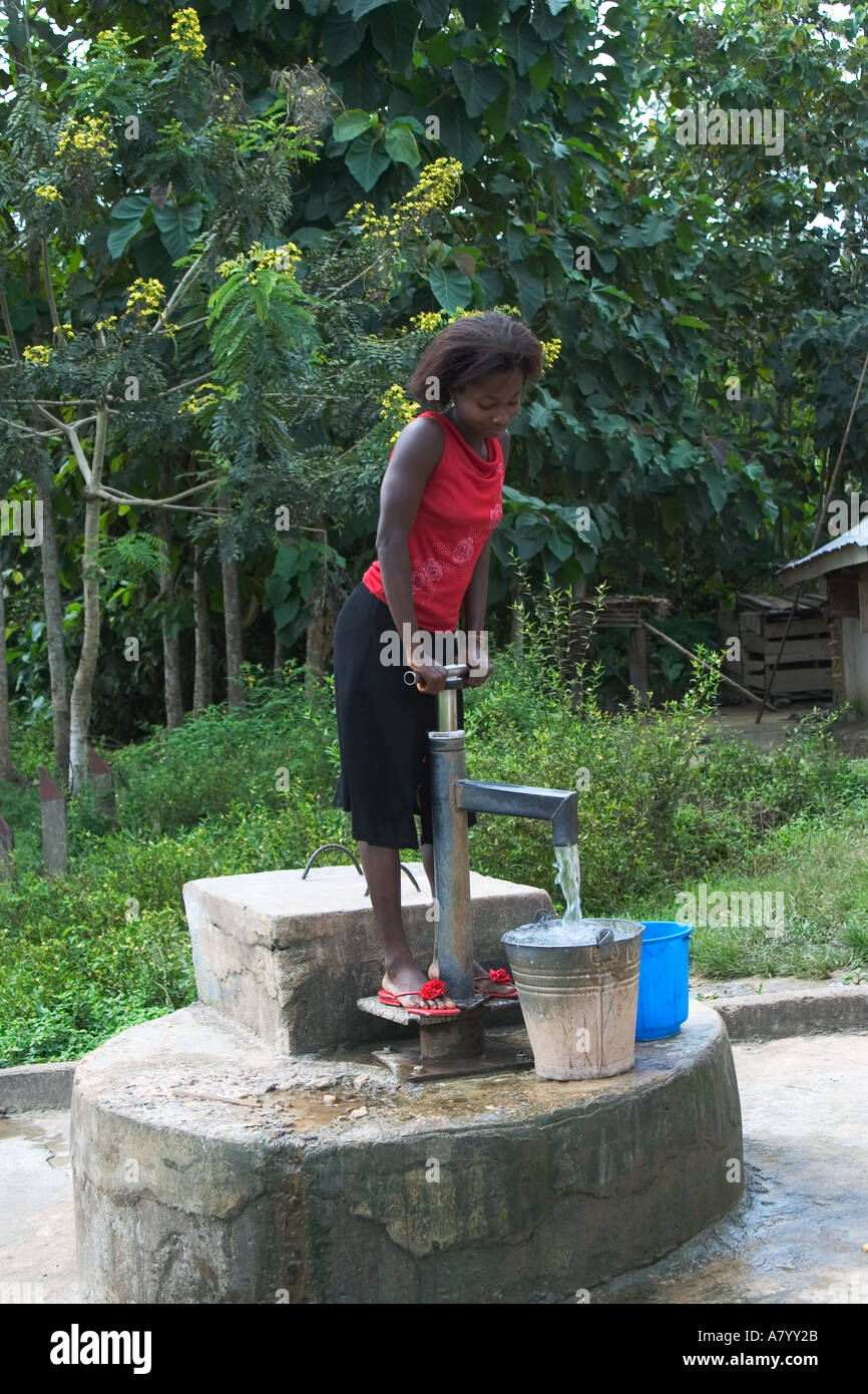 Jeune femme à l'aide de pompe à main pour le pompage d'eau potable et l'eau potable à partir de puits au centre du village de l'Afrique de l'Ouest Ghana Banque D'Images