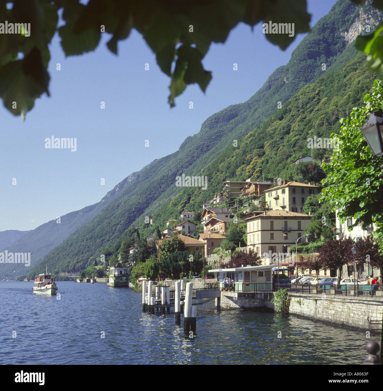 Avis de navire de plaisance au bord de lac à Argegno encadrée par les feuilles des arbres au-dessus du lac de Côme les lacs italiens Italie Europe Banque D'Images