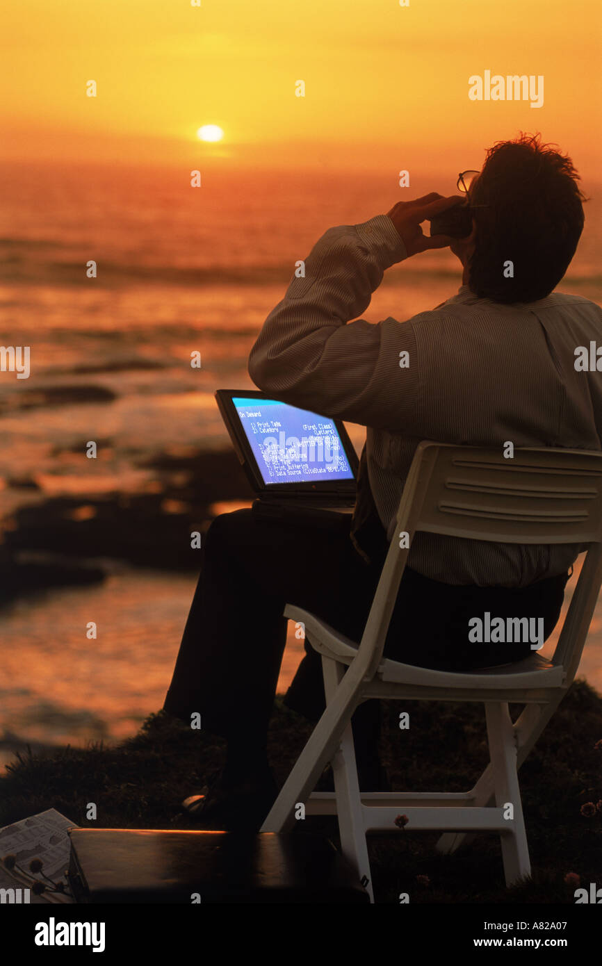 Homme avec un ordinateur portable et téléphone portable sur la côte de la Californie au coucher du soleil Banque D'Images
