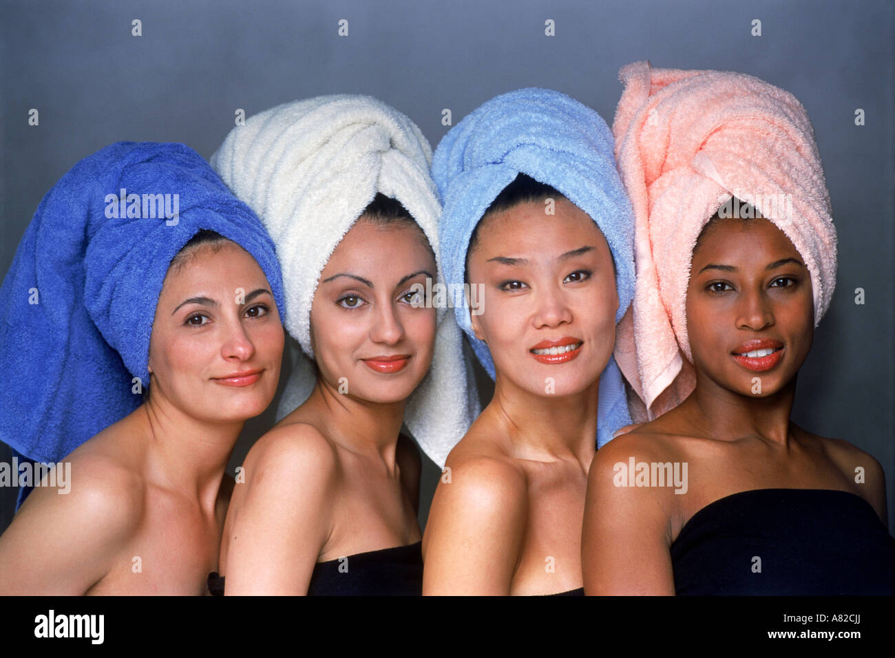 Quatre femmes de mélange ethnique avec cheveux enveloppés dans des serviettes colorées face à huis clos Banque D'Images