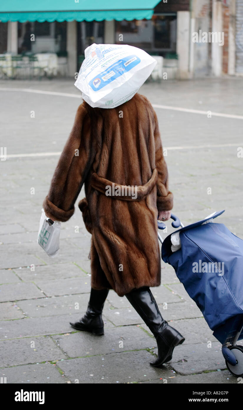 Une femme portant un manteau de fourrure protège les cheveux de la pluie avec un sac en plastique tout en marchant à travers un carré à Venise Italie Banque D'Images