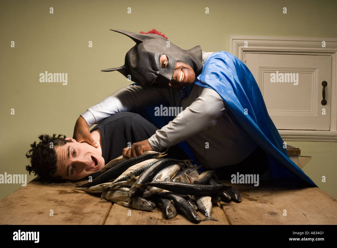 Un homme en costume de batman serrant une jeune homme sans défense le nourrir avec force le poisson. Banque D'Images