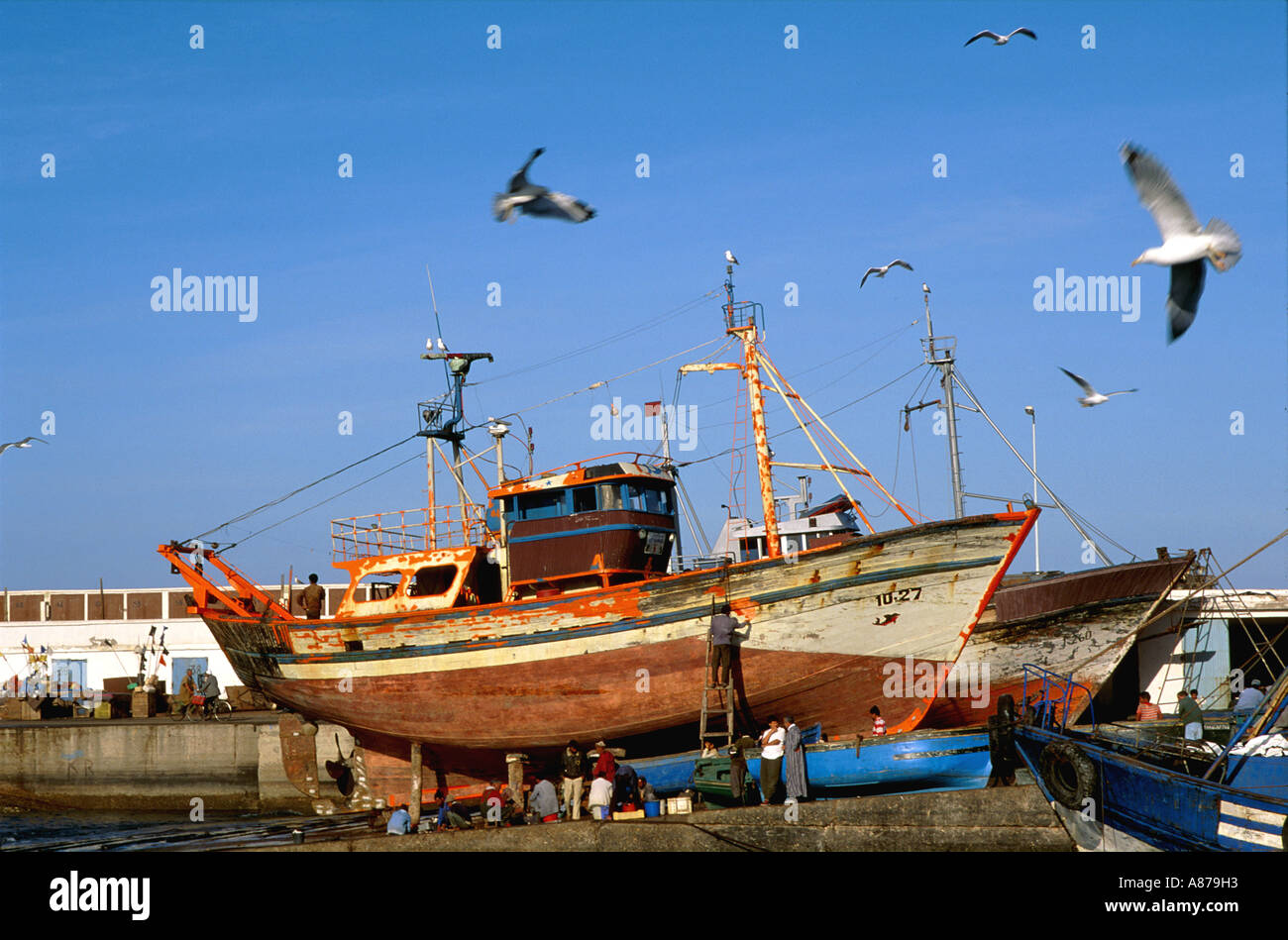 Les travailleurs qui réparent et repeignent des bateaux de pêche dans un quai sec dans le port d'Essaouira, au Maroc Banque D'Images