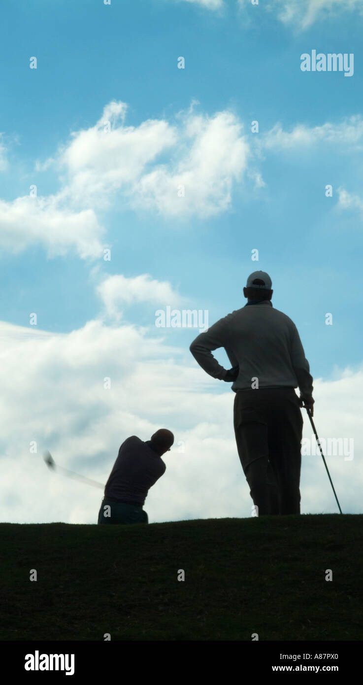 Deux golfeurs shot de derrière illustré partiront en semi en silhouette contre un ciel bleu. Banque D'Images