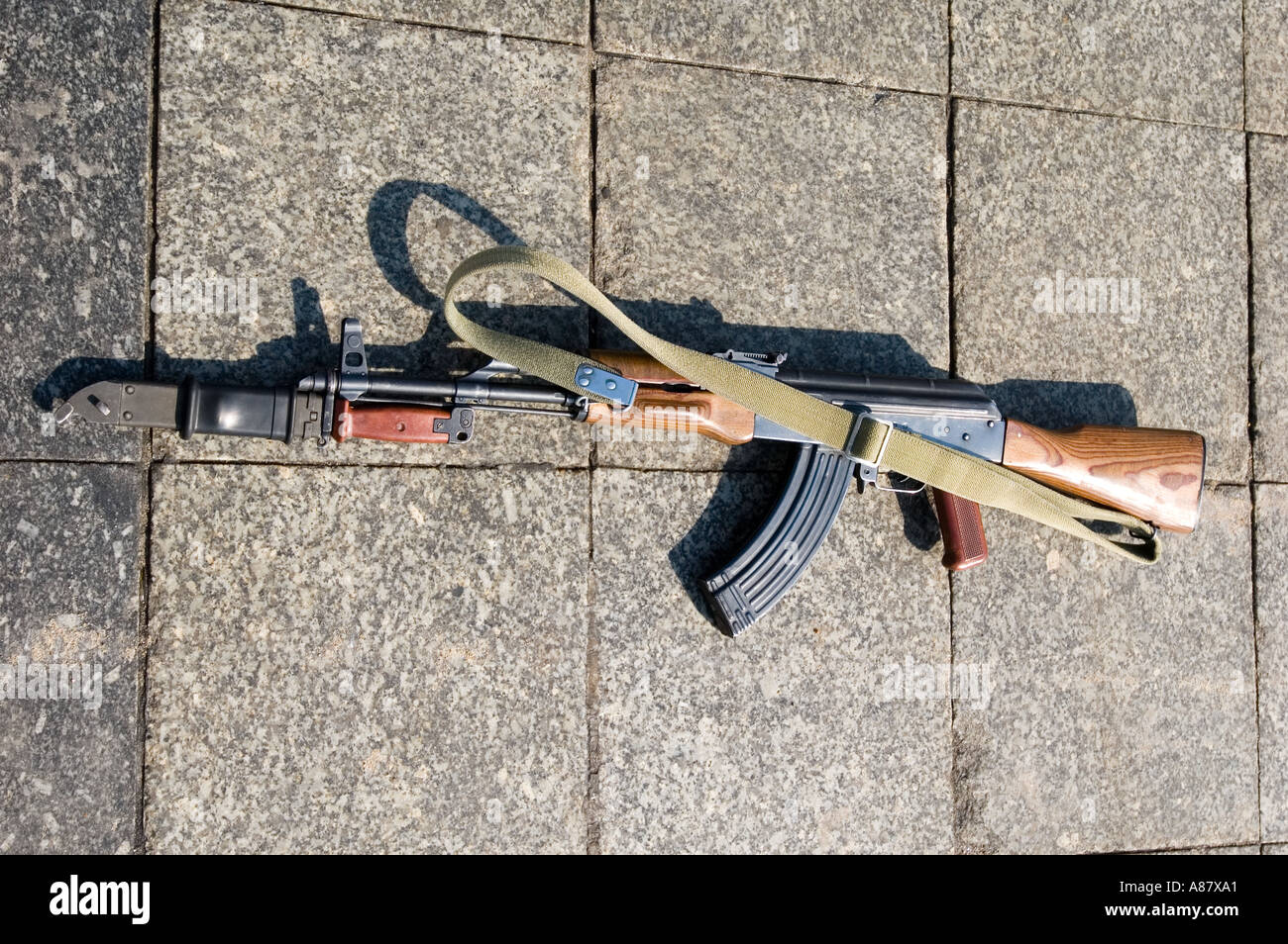 Mitrailleuse AK 47 abandonnée avec baïonnette et élingue posée sur un pavé de carreaux de pierre. Banque D'Images