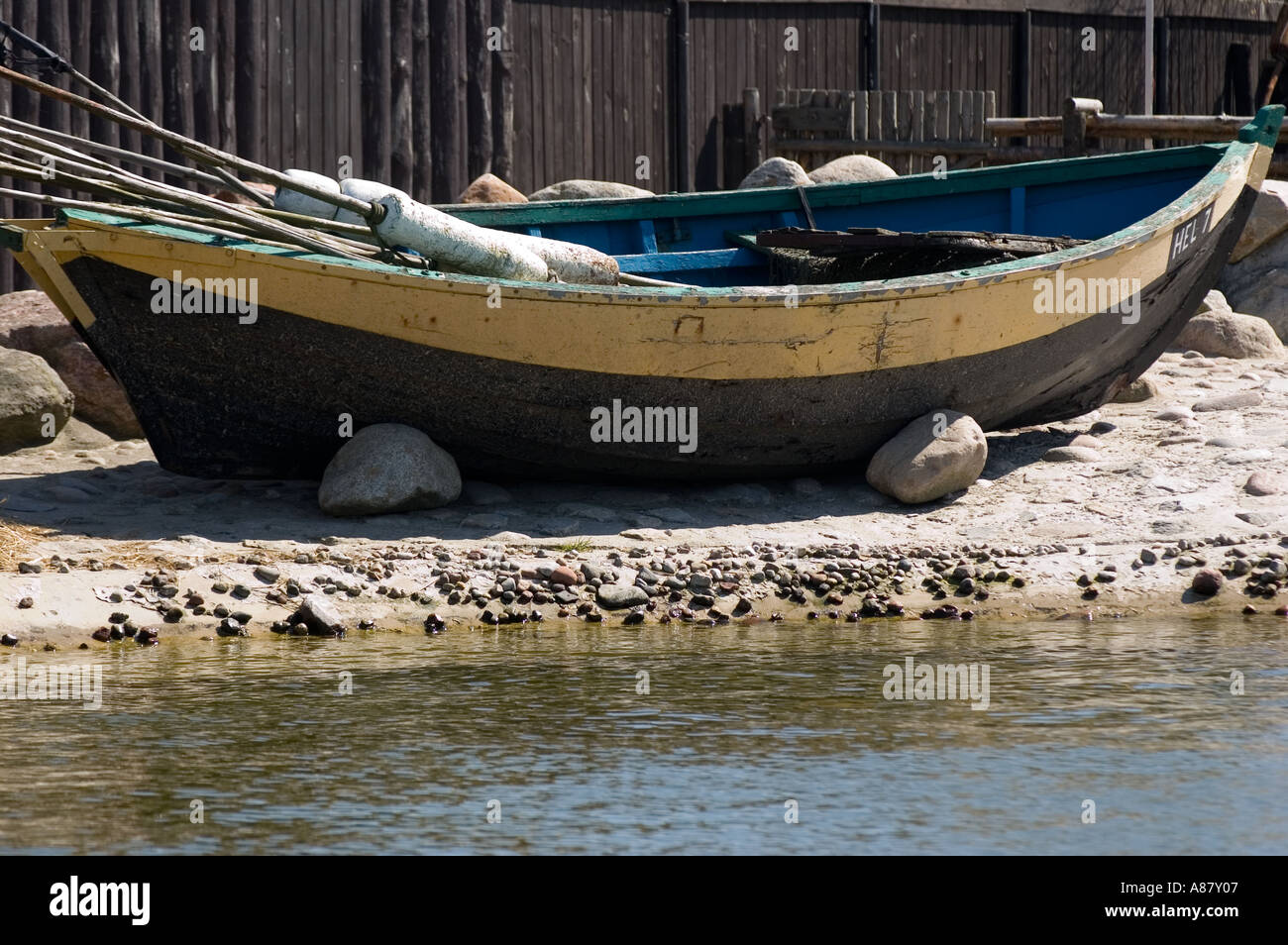 Bateau de pêcheur polonais traditionnel à coque jaune et noire reposant sur une rive rocheuse au bord de l'eau. Banque D'Images