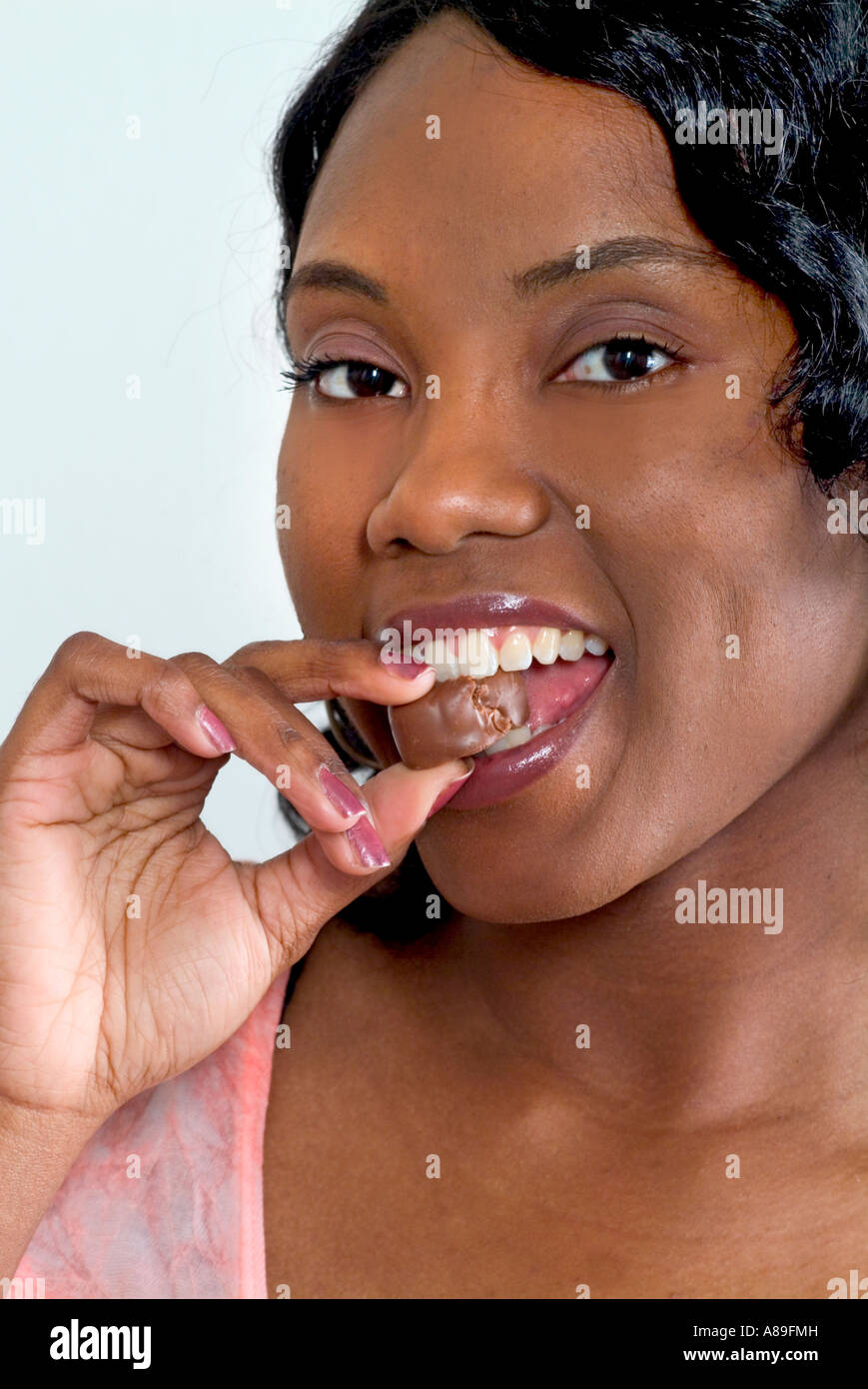 Une jolie jeune femme noire ethnique attrayant est savourant bonbons au chocolat Banque D'Images