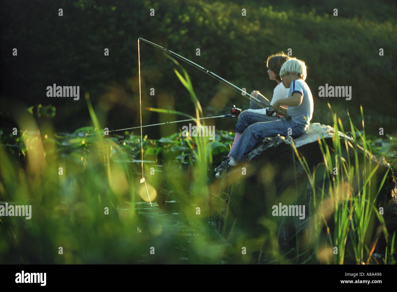 Boy and girl sitting on log pêche en étang sur côte de l'Oregon Banque D'Images