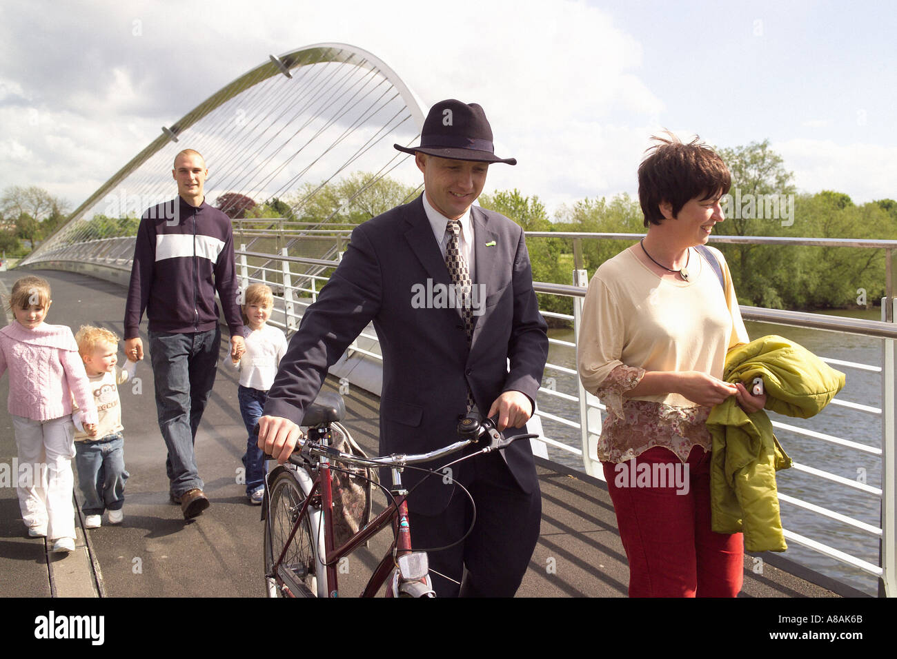 Des piétons et un jeune homme élégamment habillé portant un costume élégant et un chapeau Trilby, poussant un vélo sur le Millennium Bridge. York. Banque D'Images