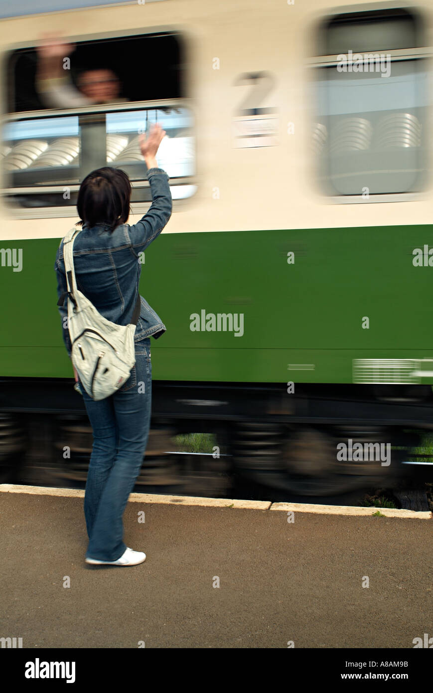 Femme debout sur une plate-forme de la gare de train au départ d'un signe avec un passager dans le train en agitant Retour Banque D'Images