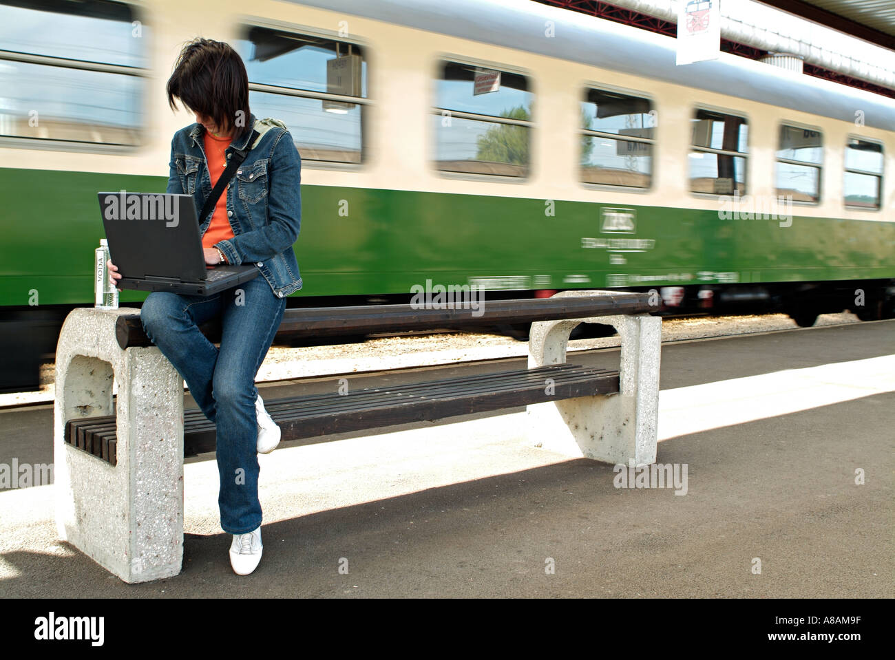 Femme assise sur un banc sur une plate-forme de la gare de la saisie sur un ordinateur portable comme un train passe Banque D'Images