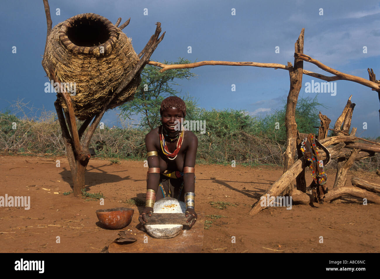 Hamer girl broyer le maïs à côté d'un grenier , Turmi, Sud Vallée de l'Omo, en Ethiopie Banque D'Images