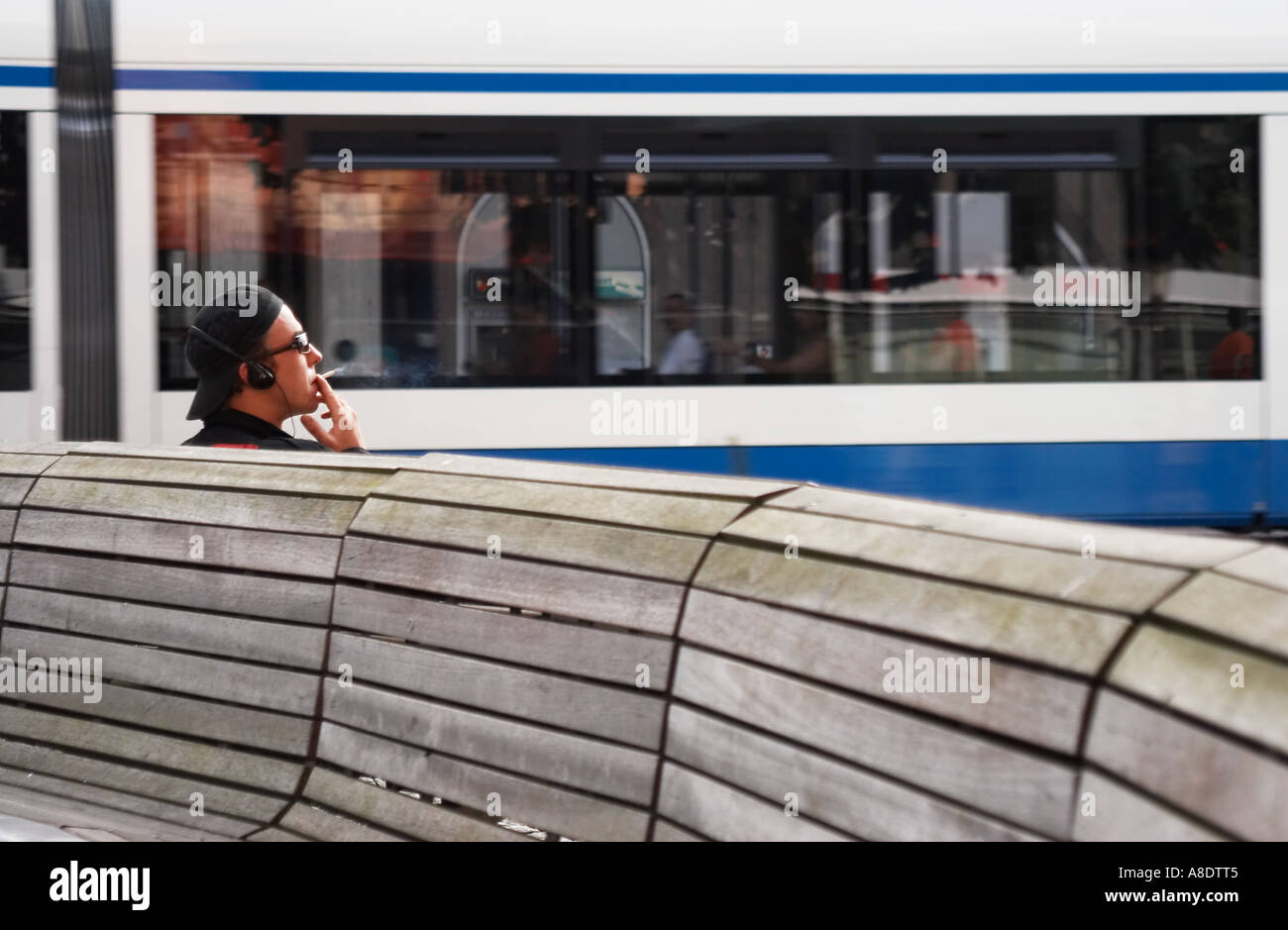 Cigarette homme assis sur un banc avec le tramway qui passe en arrière-plan Banque D'Images