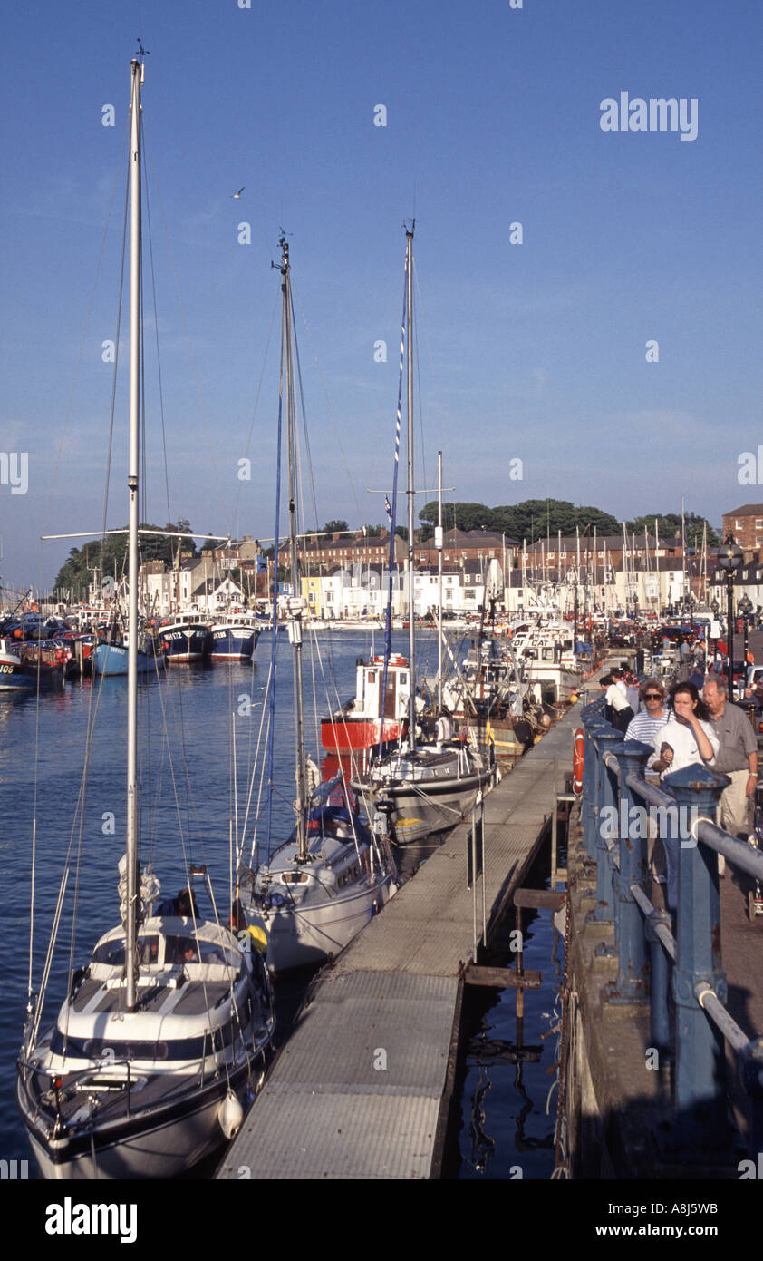 Station balnéaire de la ville gens été touristes marchant à côté de la rivière Wey et des bateaux à ponton moorings lors d'une journée de ciel bleu à Weymouth Quay Dorset Angleterre Royaume-Uni Banque D'Images
