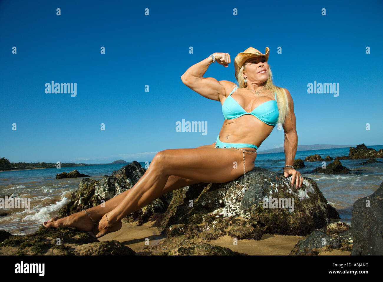 pretty-caucasian-mid-adult-woman-in-bikini-bodybuilder-sitting-on-rock