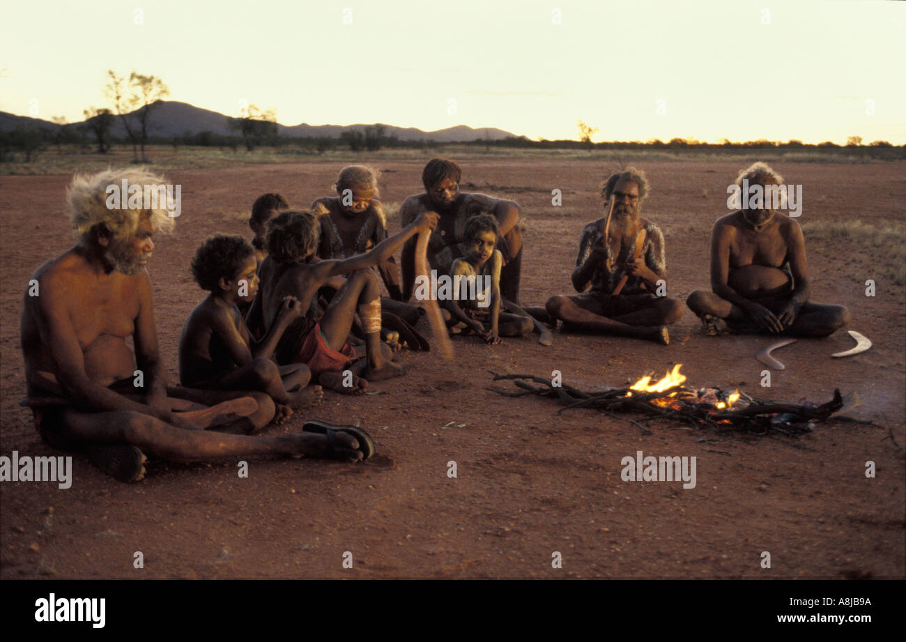 Les aînés autochtones et les jeunes garçons dans la peinture du corps de cérémonie s'asseoir sur le sable rouge par le feu après le coucher du soleil dans le désert de l'Australie centrale Banque D'Images
