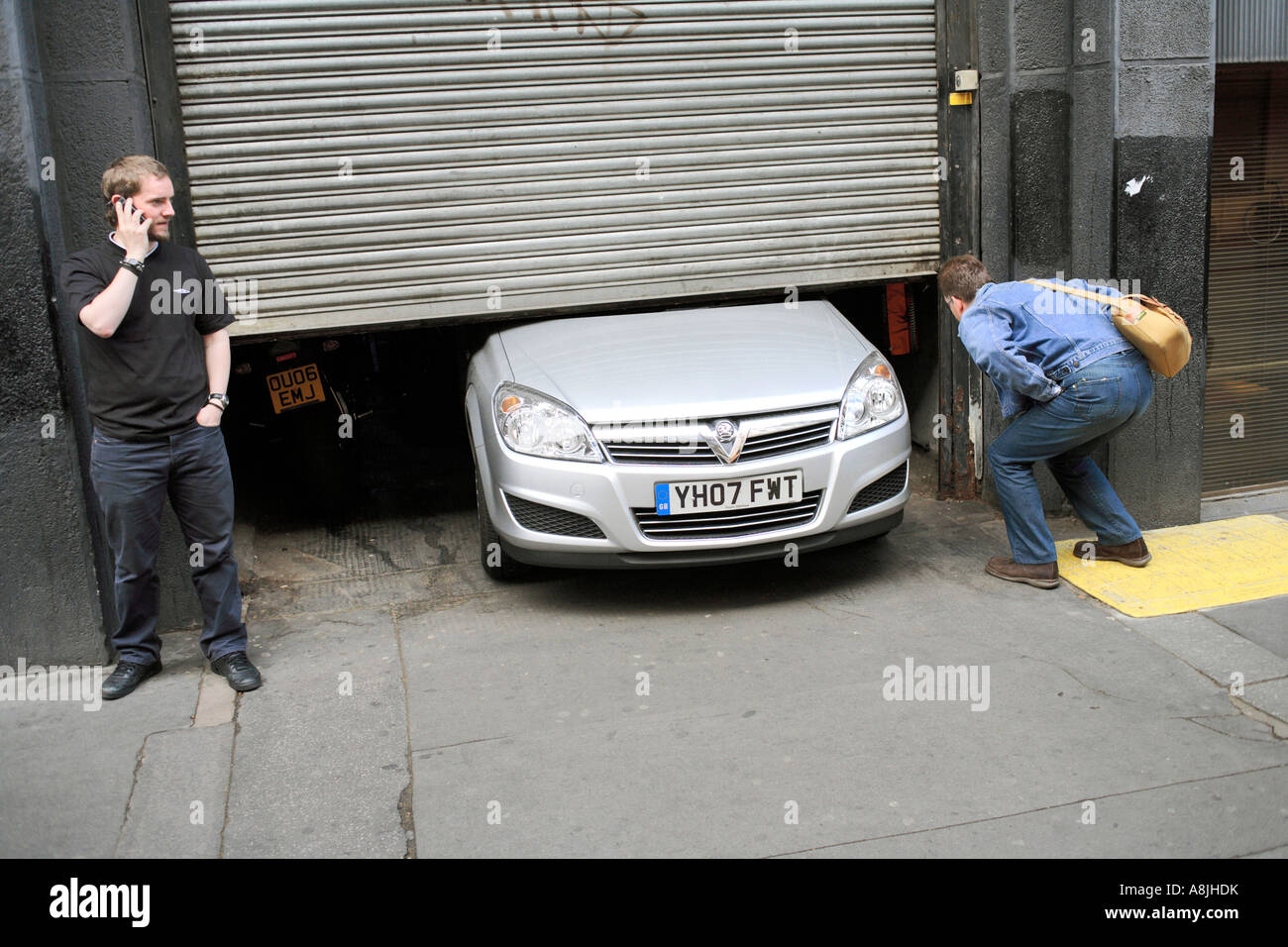 Deux hommes à la recherche sur une voiture pris sous une porte de garage à Londres Banque D'Images