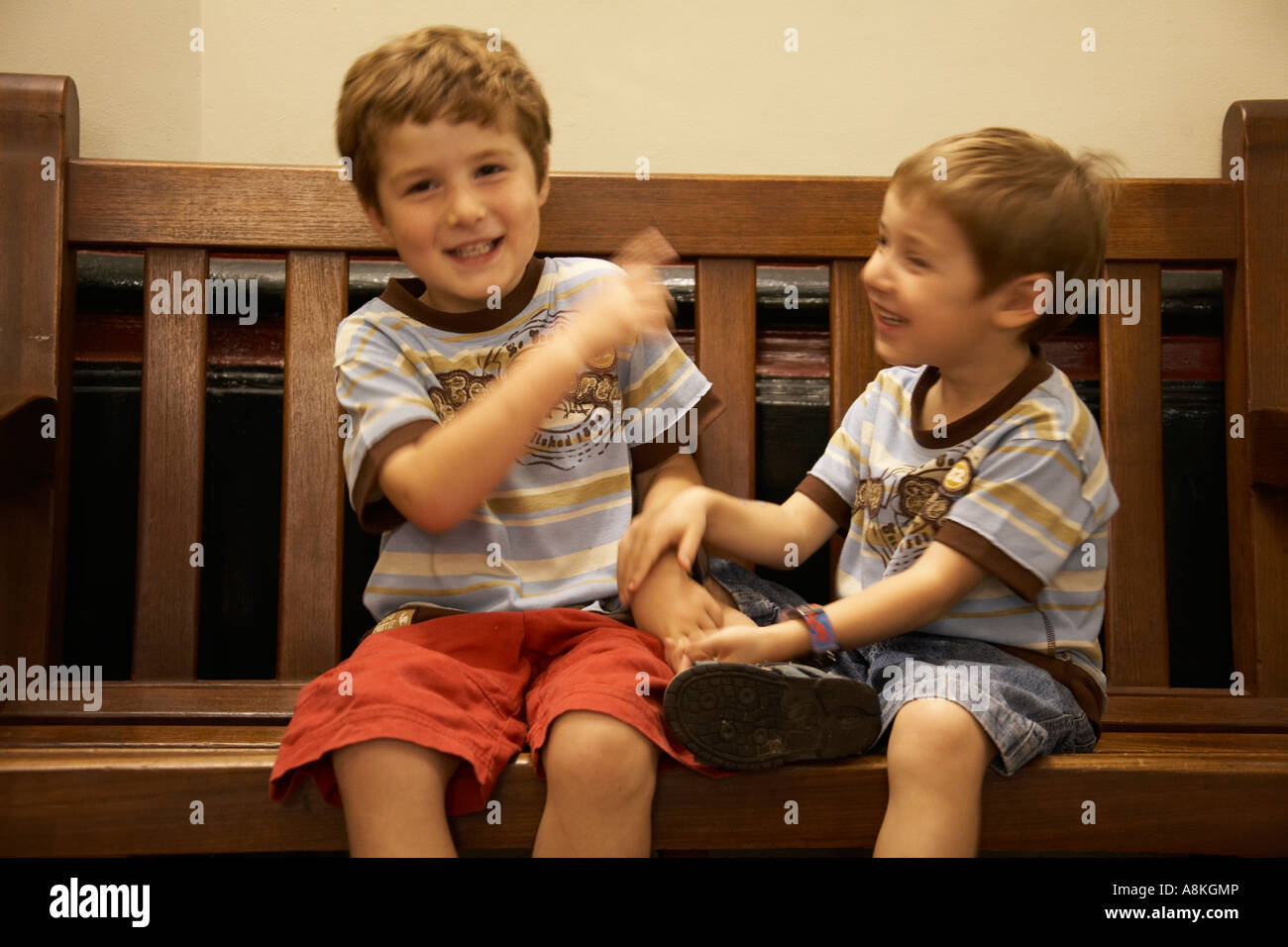Deux jeunes garçons enfants frères portant des shorts et T shirts assis sur  un banc à rire de combat Photo Stock - Alamy