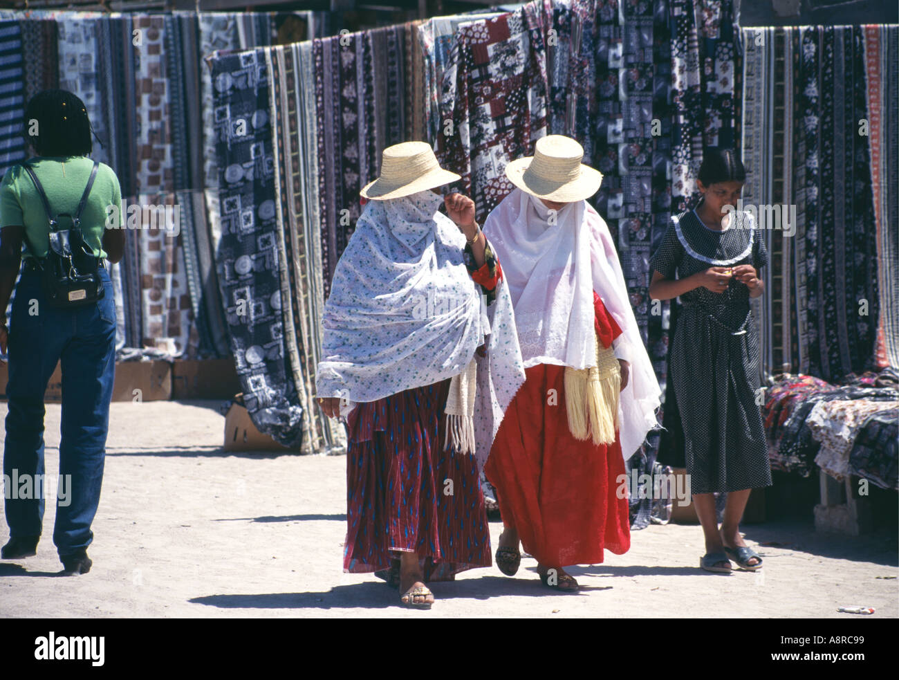 Leurs caractéristiques obscurci par l'écoulement de châles et de larges chapeaux chapeau de paille deux femmes locales à flâner au soleil passé les produits exposés à la vente sur le marché de Houmt Souk produire sur l'île de Djerba Tunisie Banque D'Images