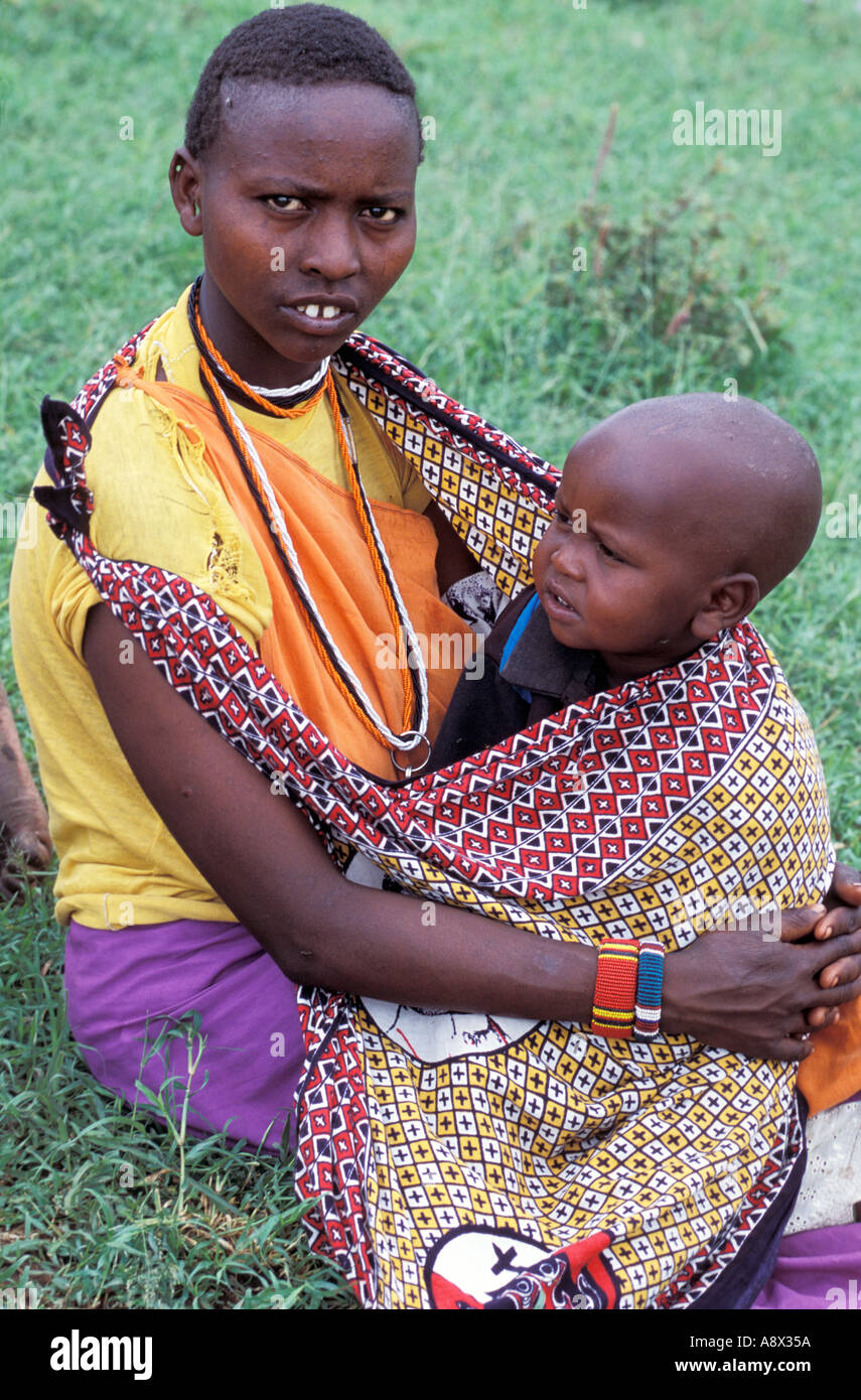 Afrique Kenya Masai Mara National Reserve Masai jeune mère en vêtements traditionnels et bijoux avec des tout-petits Banque D'Images