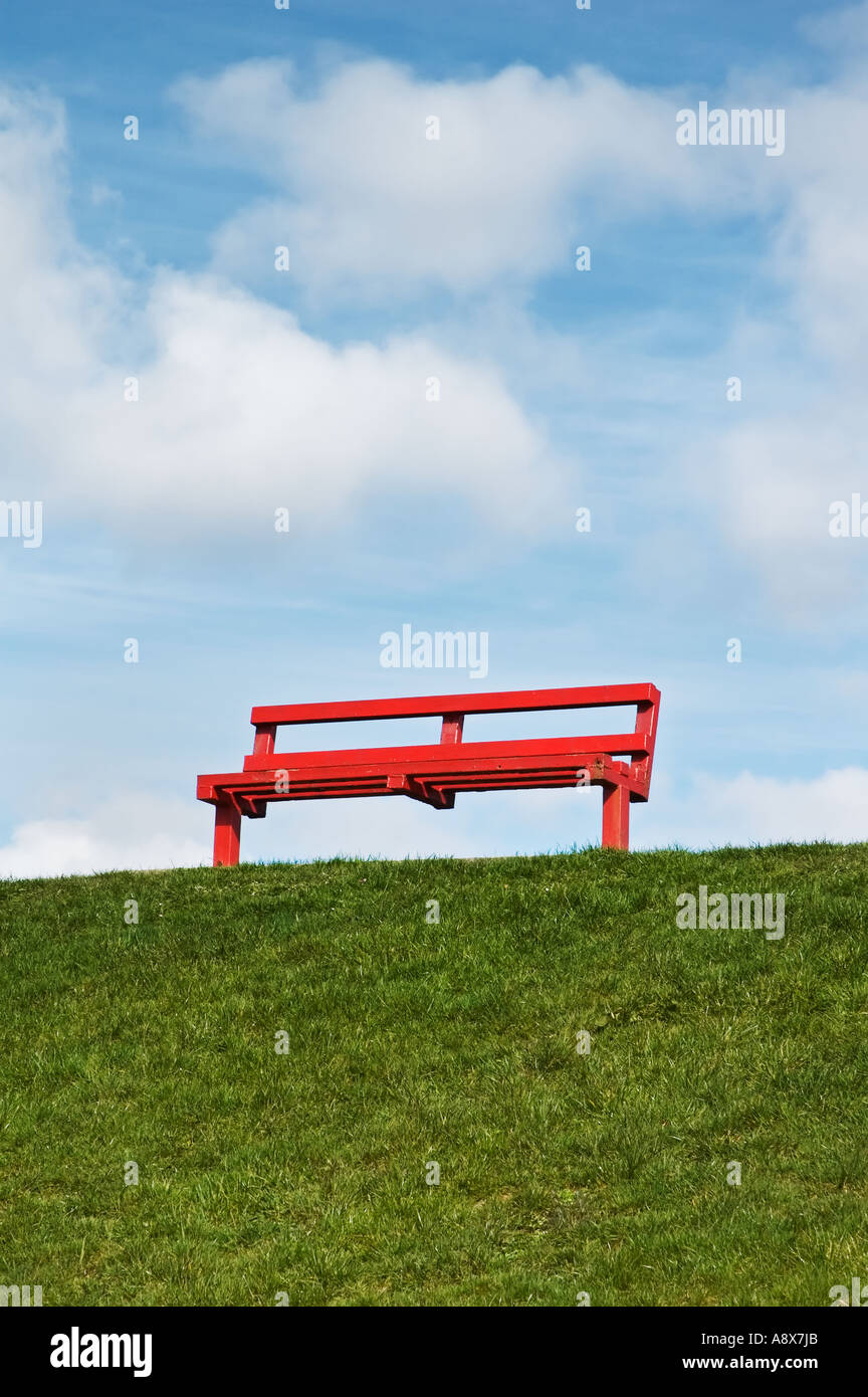 Un fauteuil rouge / banc dans un champ avec un bleu ciel nuageux dans l'arrière-plan. Banque D'Images