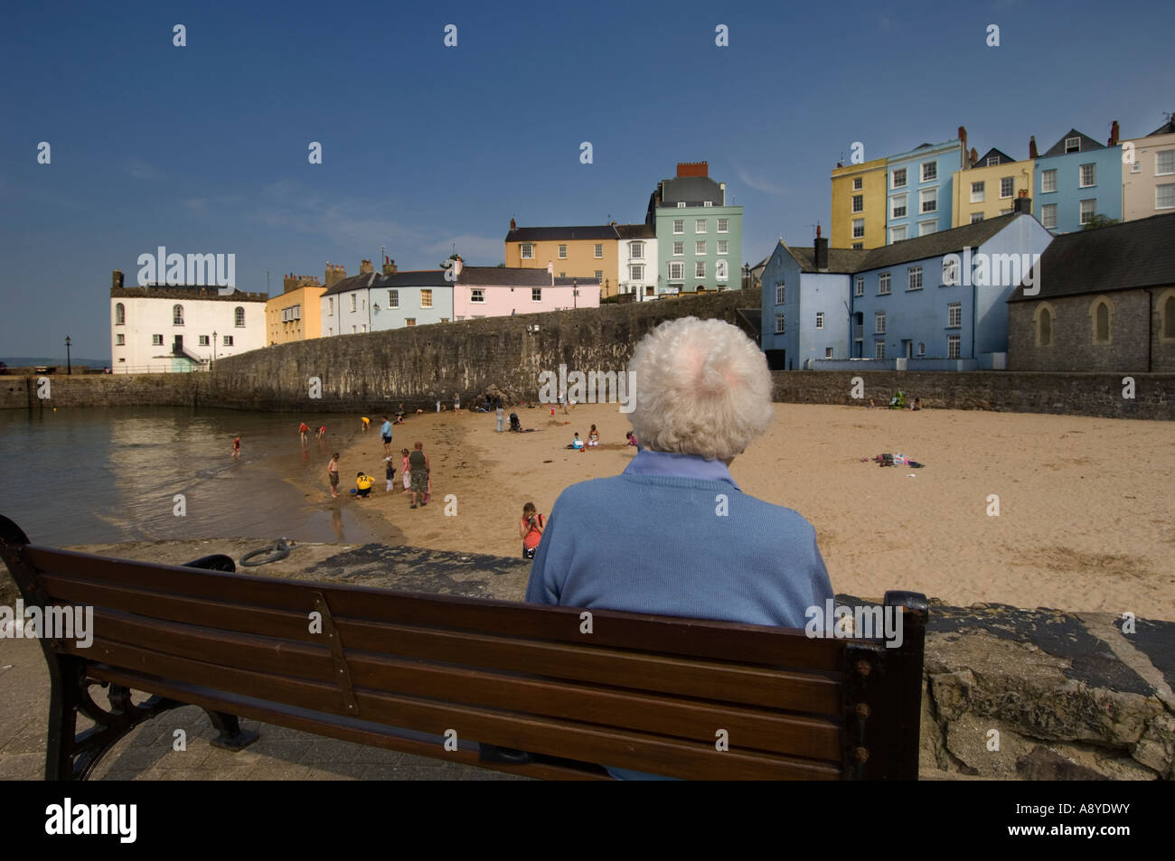 Le Pays de Galles à Cardiff - vieille femme assise toute seule sur un banc seul regardant les personnes jouant sur la plage sur l'après-midi d'été Banque D'Images