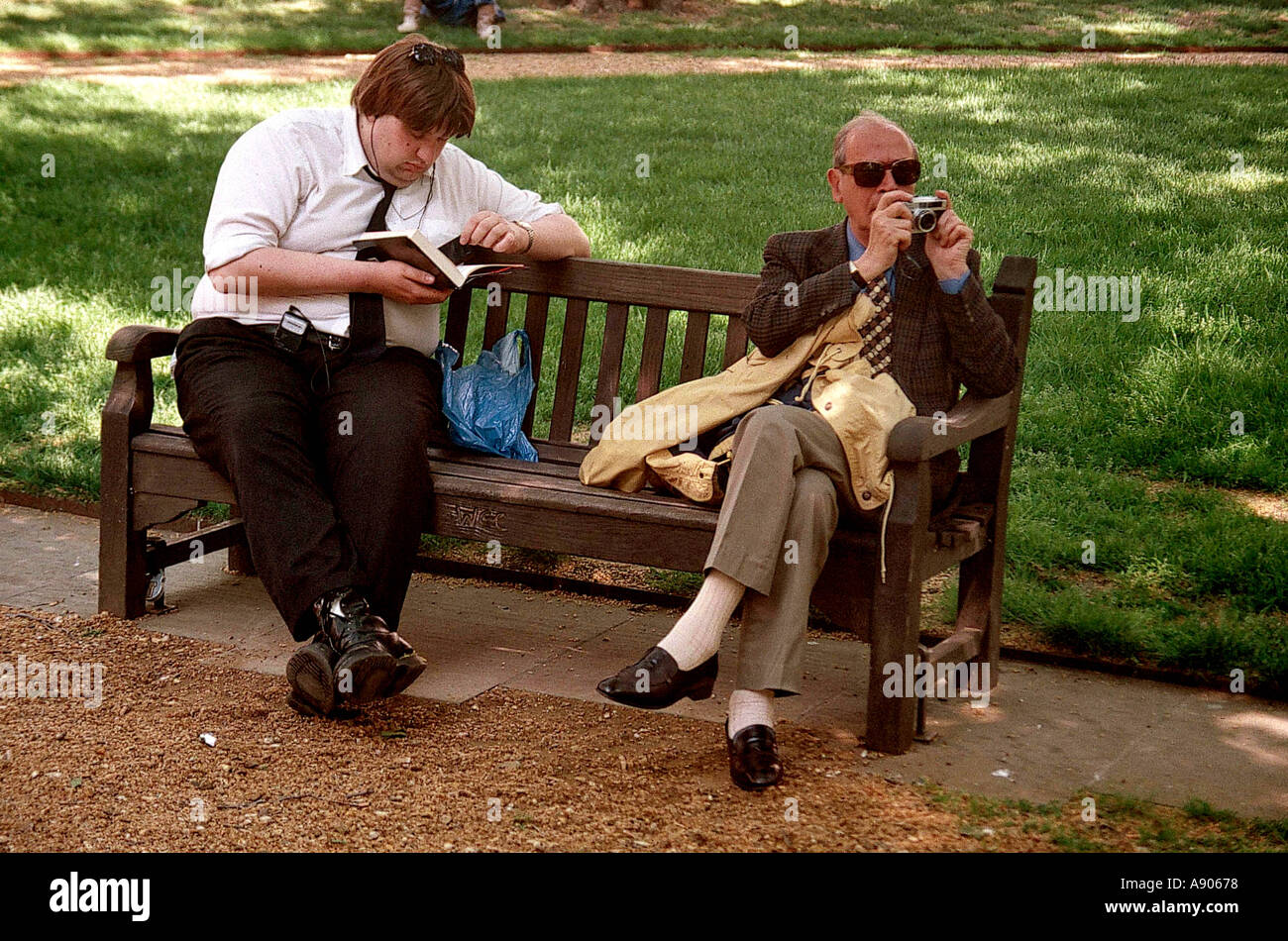 Deux hommes assis sur le banc de parc lire et prendre des photographies Banque D'Images