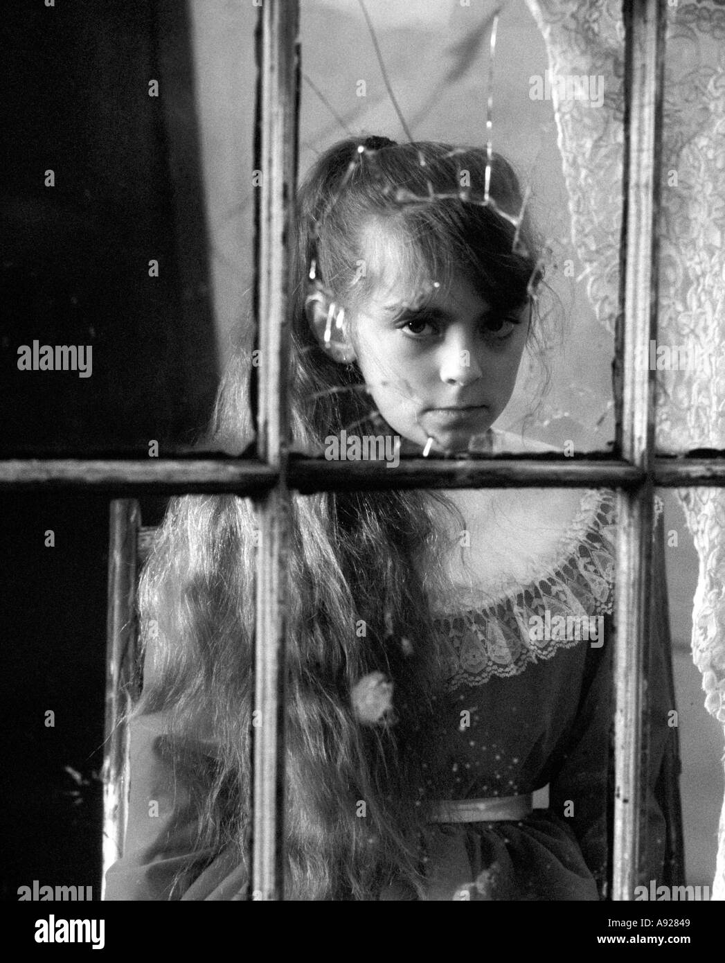 Petite fille à la fenêtre en verre craquelé, noir et blanc, se recroquevillant, regard sévère, regardant, antique, ancien, Banque D'Images