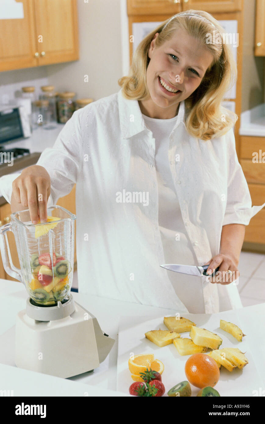 Portrait d'une jeune femme enceinte, mettre les tranches de fruits dans un processeur de nourriture Banque D'Images
