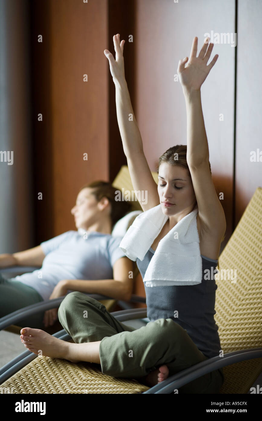 Les jeunes femmes vous relaxant dans des chaises longues, une seule séance de style indien avec bras levés et les yeux fermés Banque D'Images