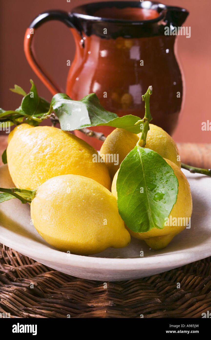 Citrons frais avec des feuilles sur la plaque en face de pot en terre cuite FoodCollection Banque D'Images