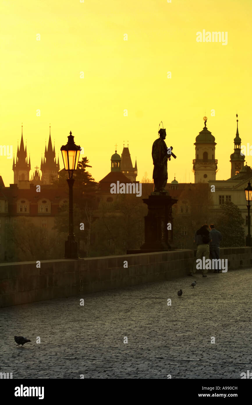 L'heure d'or baigne l'emblématique pont Charles de Prague dans une lueur chaleureuse, tandis que des statues aux silhouettes montent la garde sur la scène matinale sereine Banque D'Images