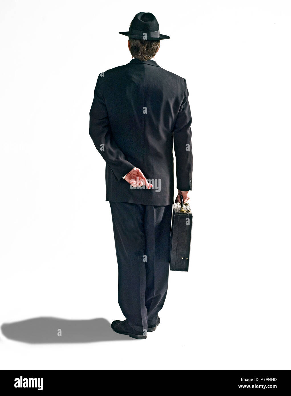 L'homme d'affaires en costume noir avec chapeau fedora noir et porte-documents avec les doigts croisés derrière le dos Banque D'Images