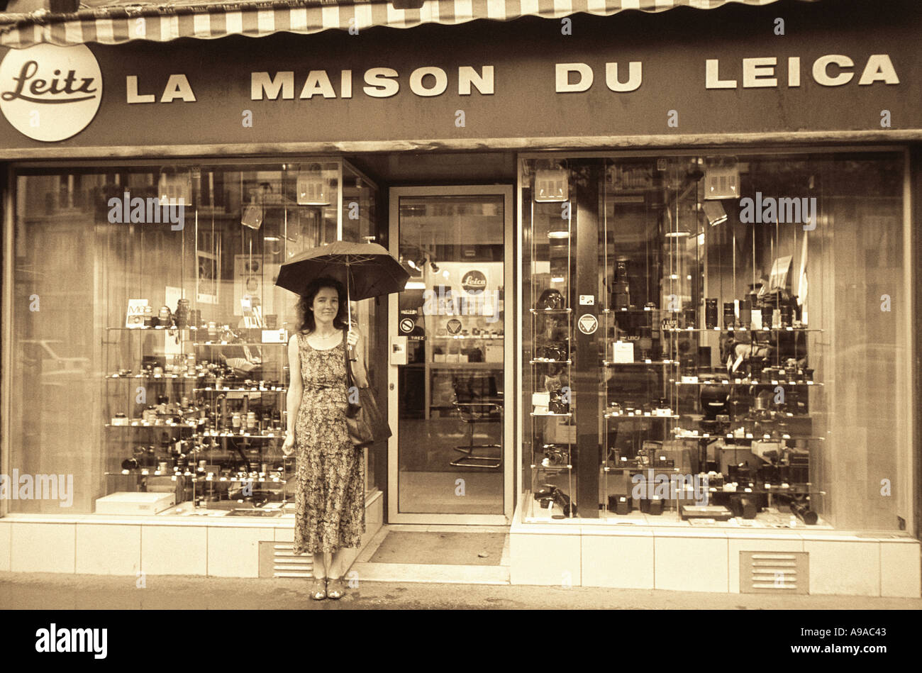 Le noir et blanc d'une jeune femme debout en face de la Maison du Leica Camera shop à Paris sous son parapluie Banque D'Images