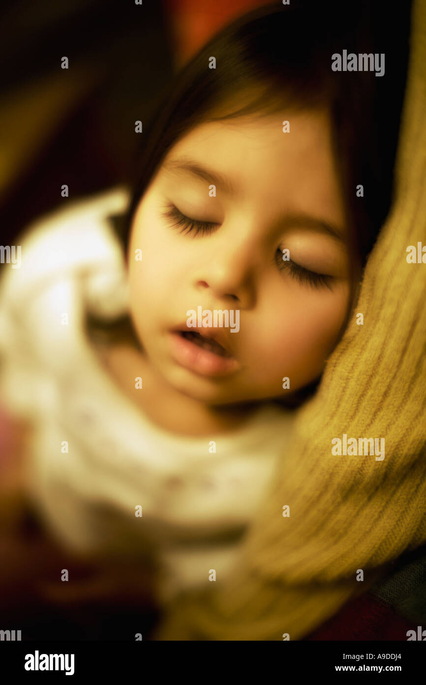 Head and shoulders portrait de fillette de deux ans dormant dans les bras de sa mère Banque D'Images